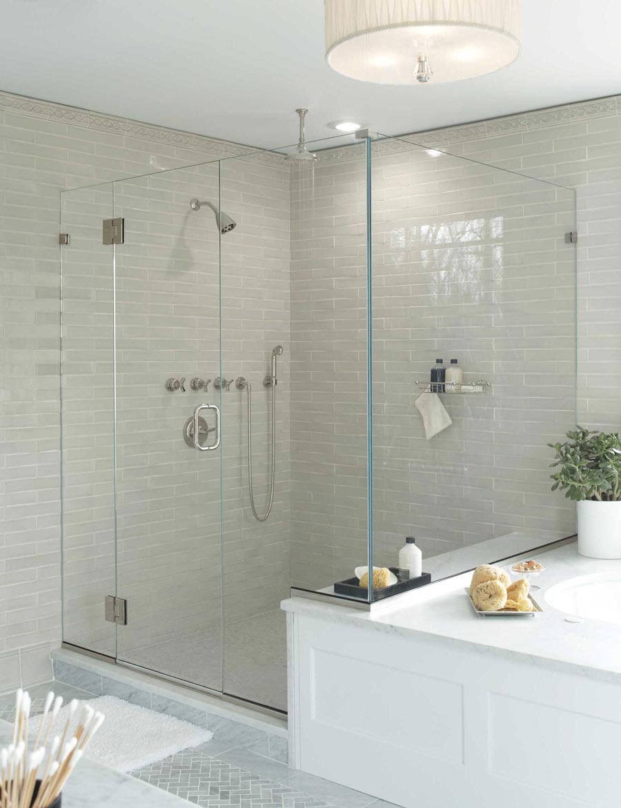 Frameless corner stall shower enclosure with hinges and a pull handle next to a large tiled soaking tub.