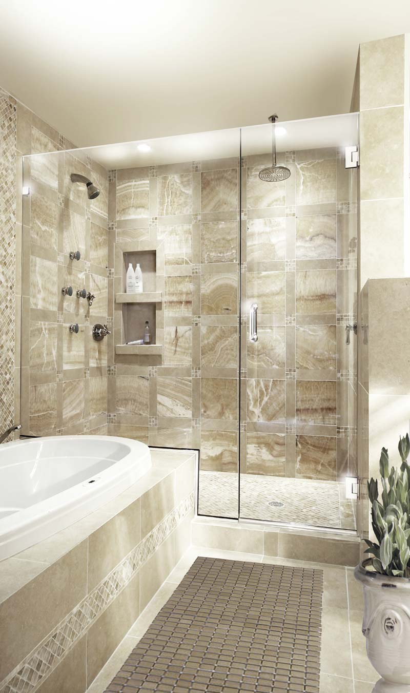 Frameless glass shower enclosure behind a tiled tub. There are toiletries visible through the transparent glass doors.