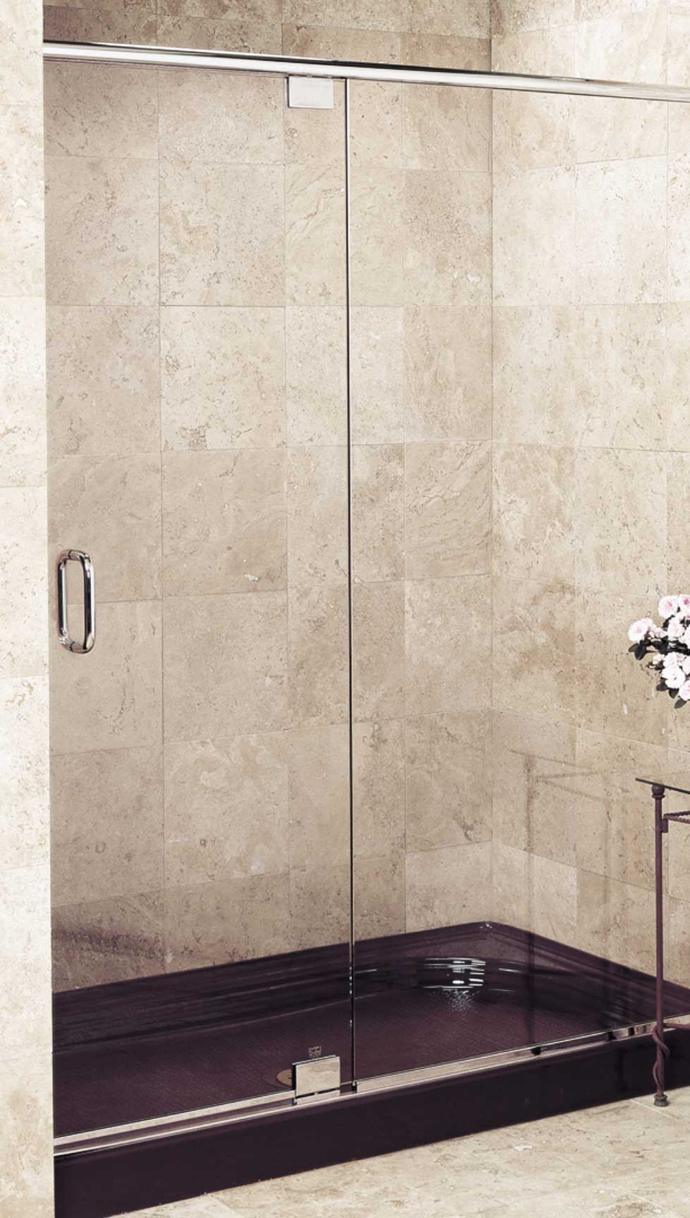 Frameless shower enclosure with a tubular pull handle and a pivot hinged door. Sand-colored tile and a purple basin.
