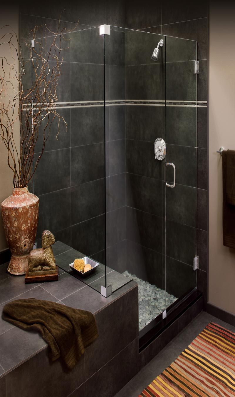 Minimalist shower enclosure without frame or channels and silver pull handle. Large clamps affix glass to dark tile wall.