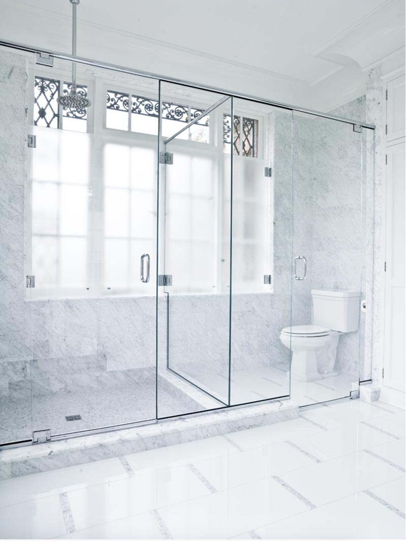 Wall to wall frameless glass enclosure with both a shower and toilet stall. Each all-glass stall has a pull handle.