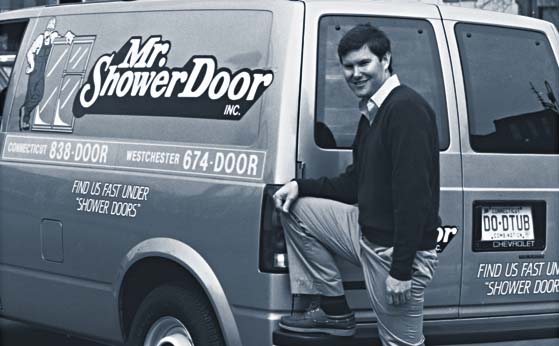Tom Whitaker, founder of Mr. Shower Door, standing with his leg up on the bumper of the original Mr. Shower Door service van.