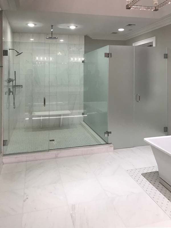 Wall to wall frameless glass enclosure with a transparent glass walk-in shower and an acid-etched toilet stall.